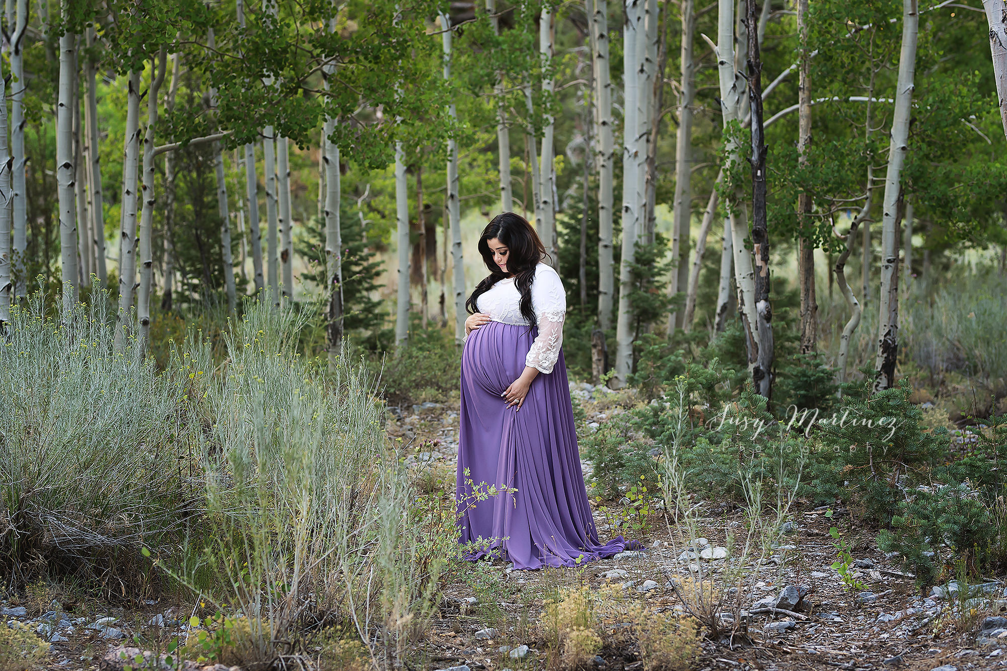 pose holds belly in purple dress during mountain maternity portraits