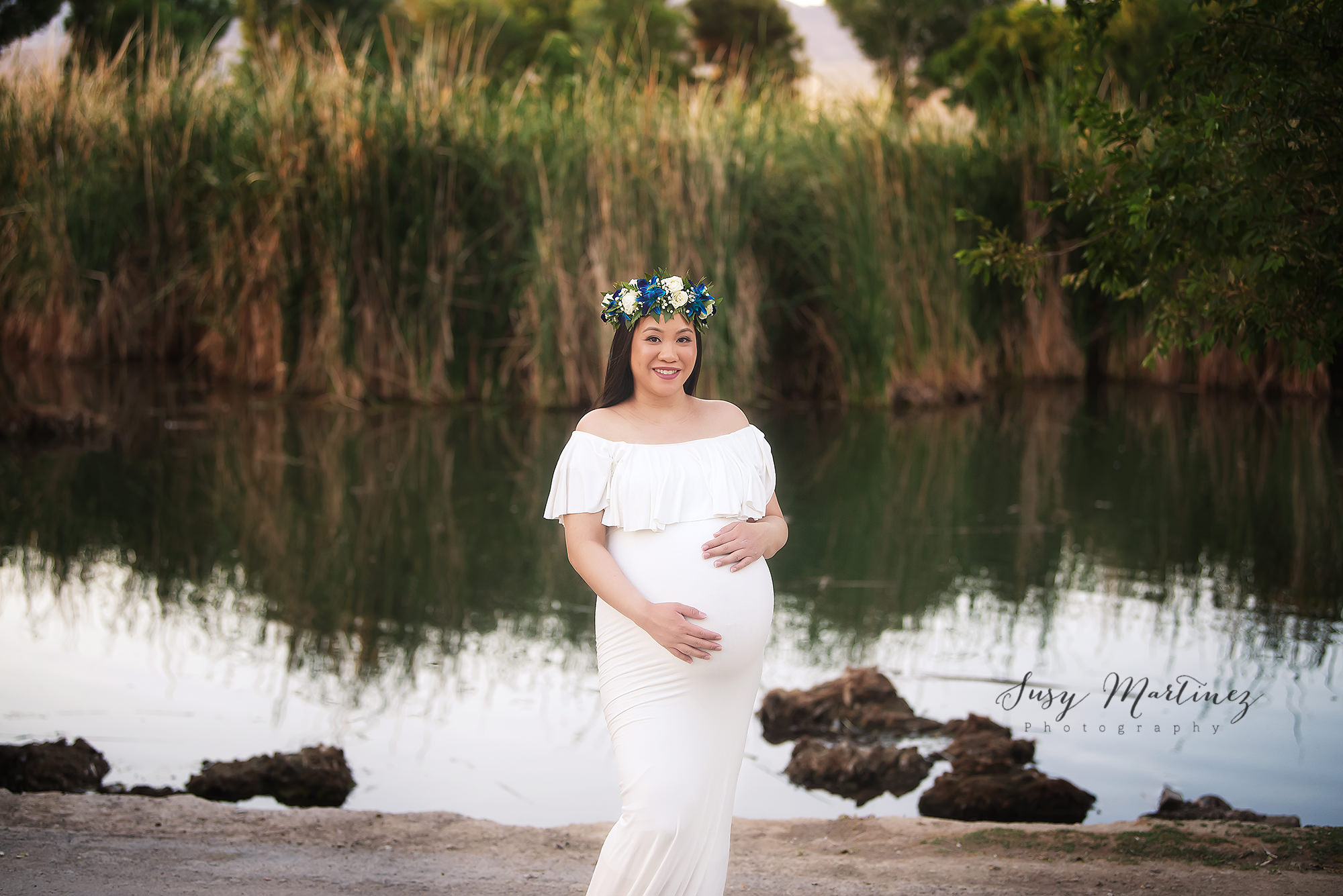 mom in white Sew Trendy Accessories gown with flower crown poses by lake in Nevada park