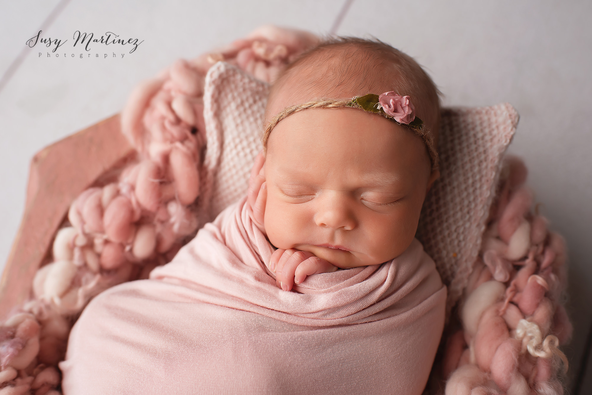 baby sleeps in pink wrap curled up on knit blanket