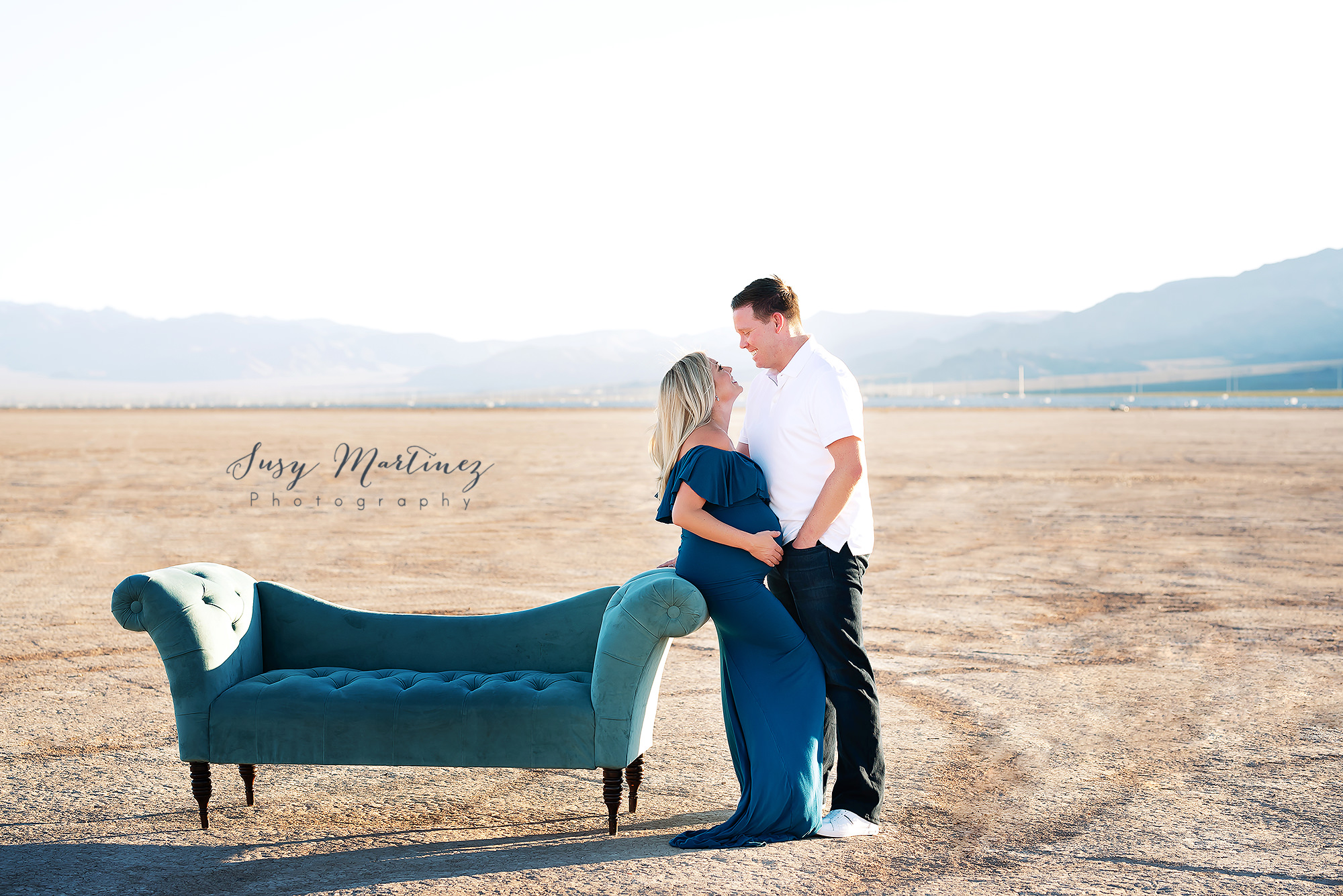 couple leans against teal couch during Dry Lake Bed maternity session
