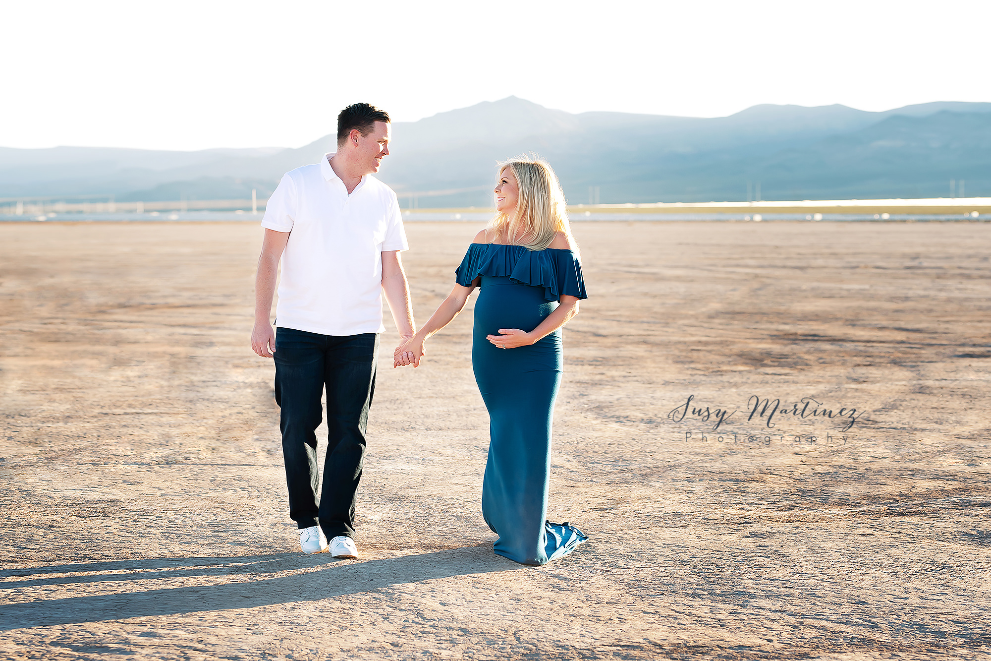 expecting couple holds hands walking through Las Vegas lake bed