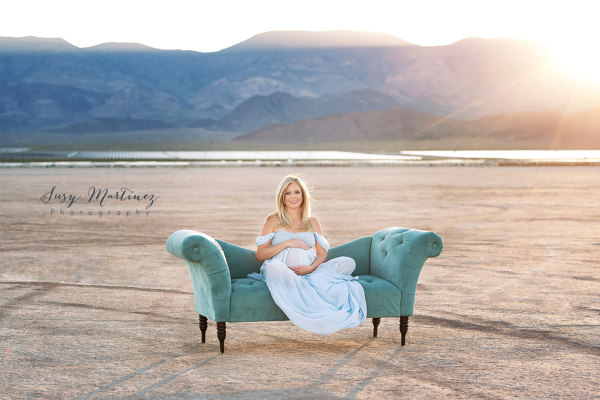 mom sits on teal couch in dry Lake Bed during maternity photos