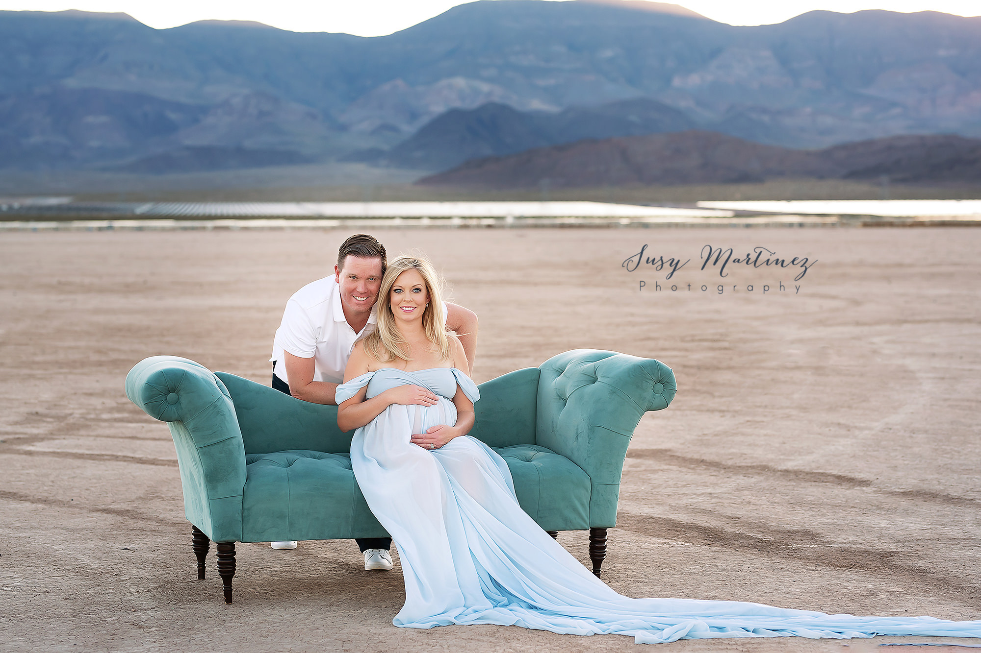mom holds belly sitting on teal couch during Dry Lake Bed maternity session