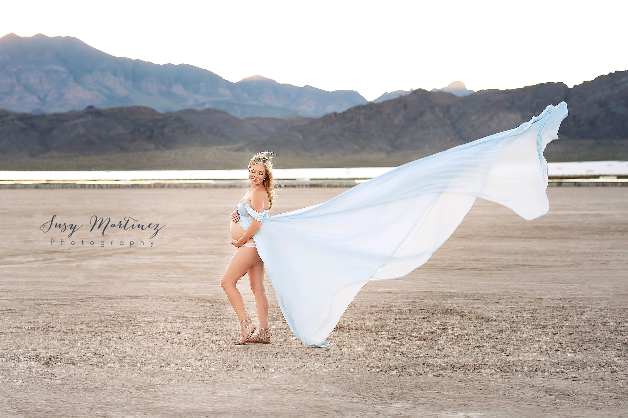 mom holds belly while skirt floats in the air during Dry Lake Bed maternity session
