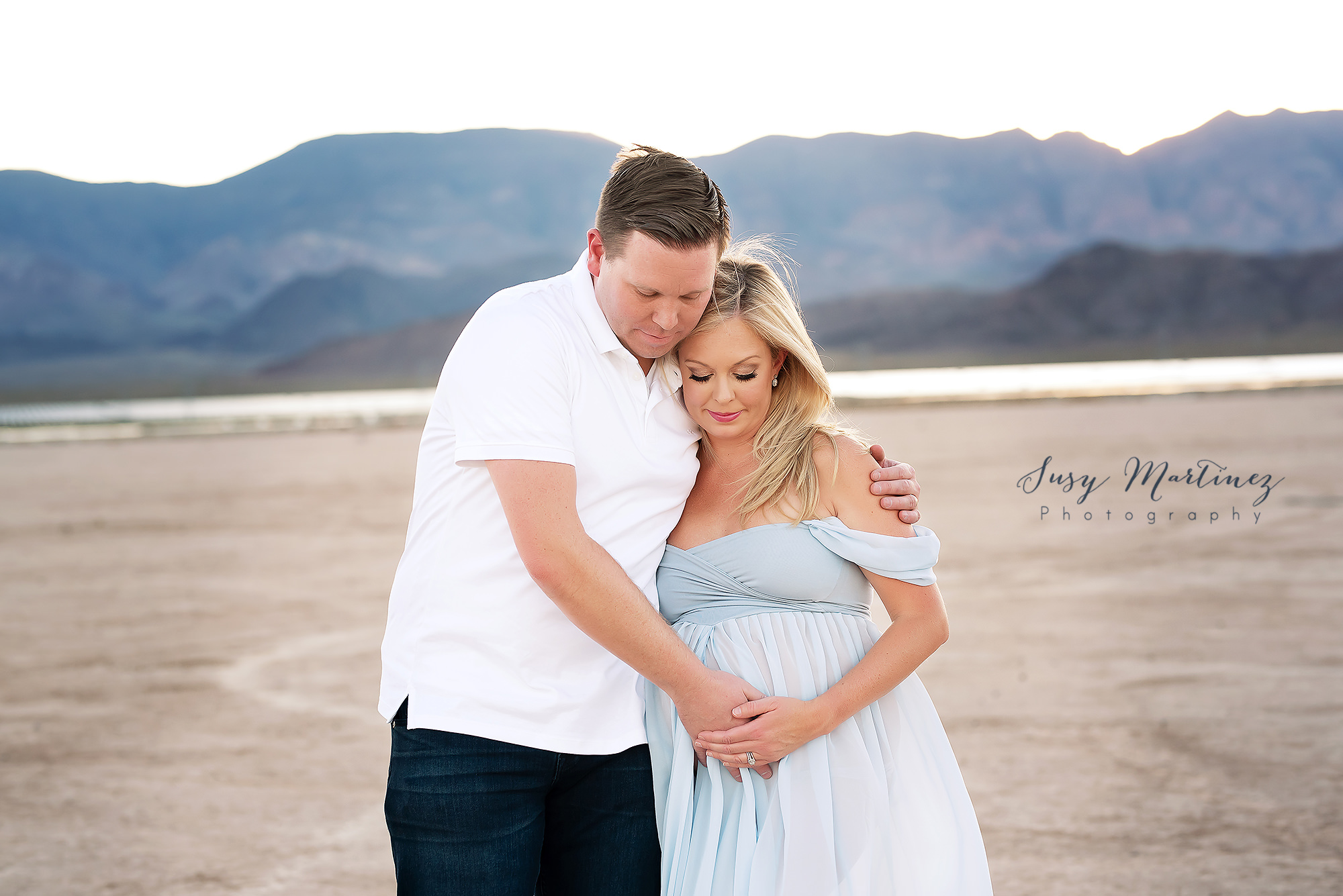 parents hug and look down at baby in belly during Dry Lake Bed maternity session
