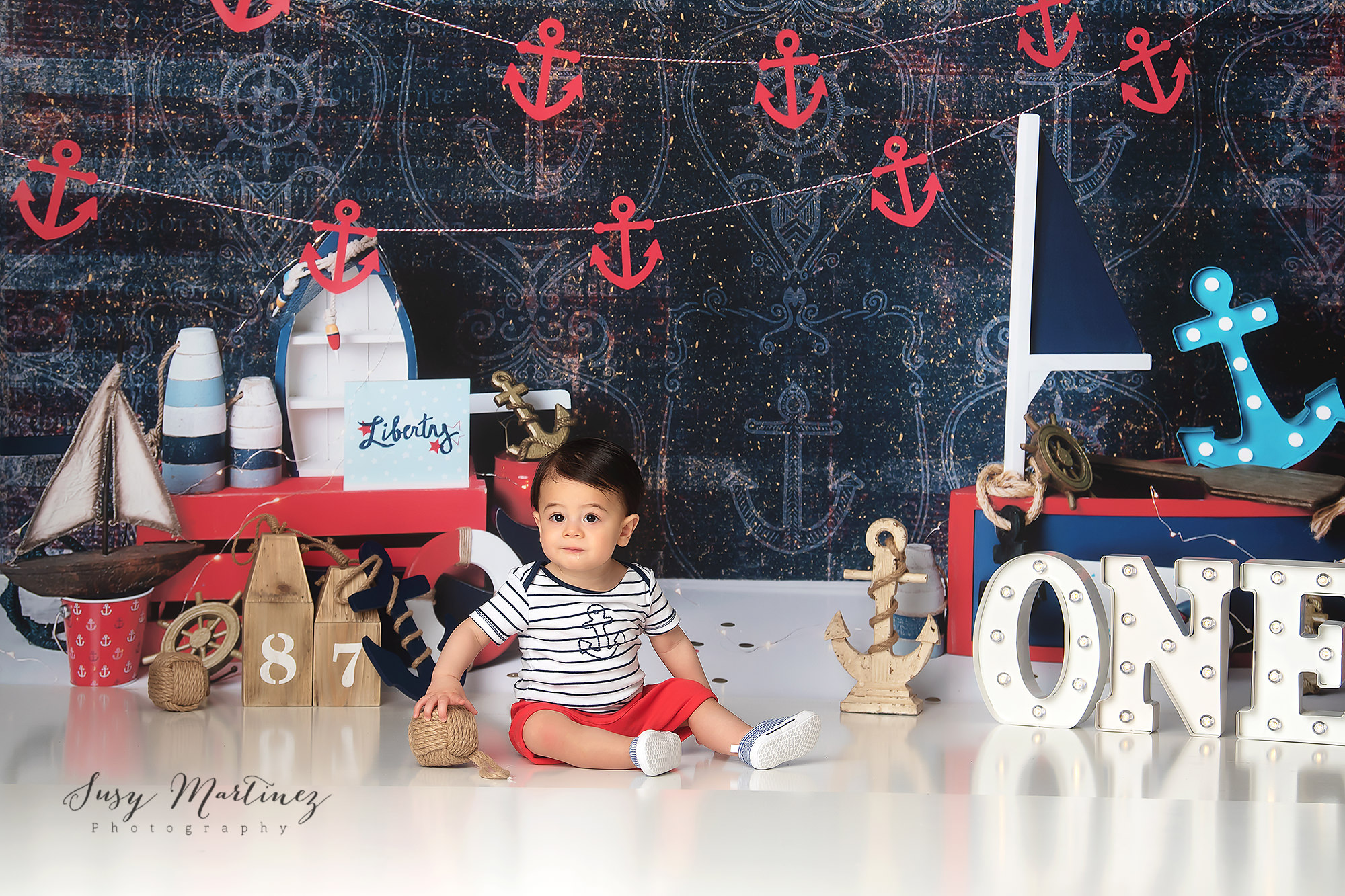 milestone portraits of one year old in front of red and blue nautical backdrop
