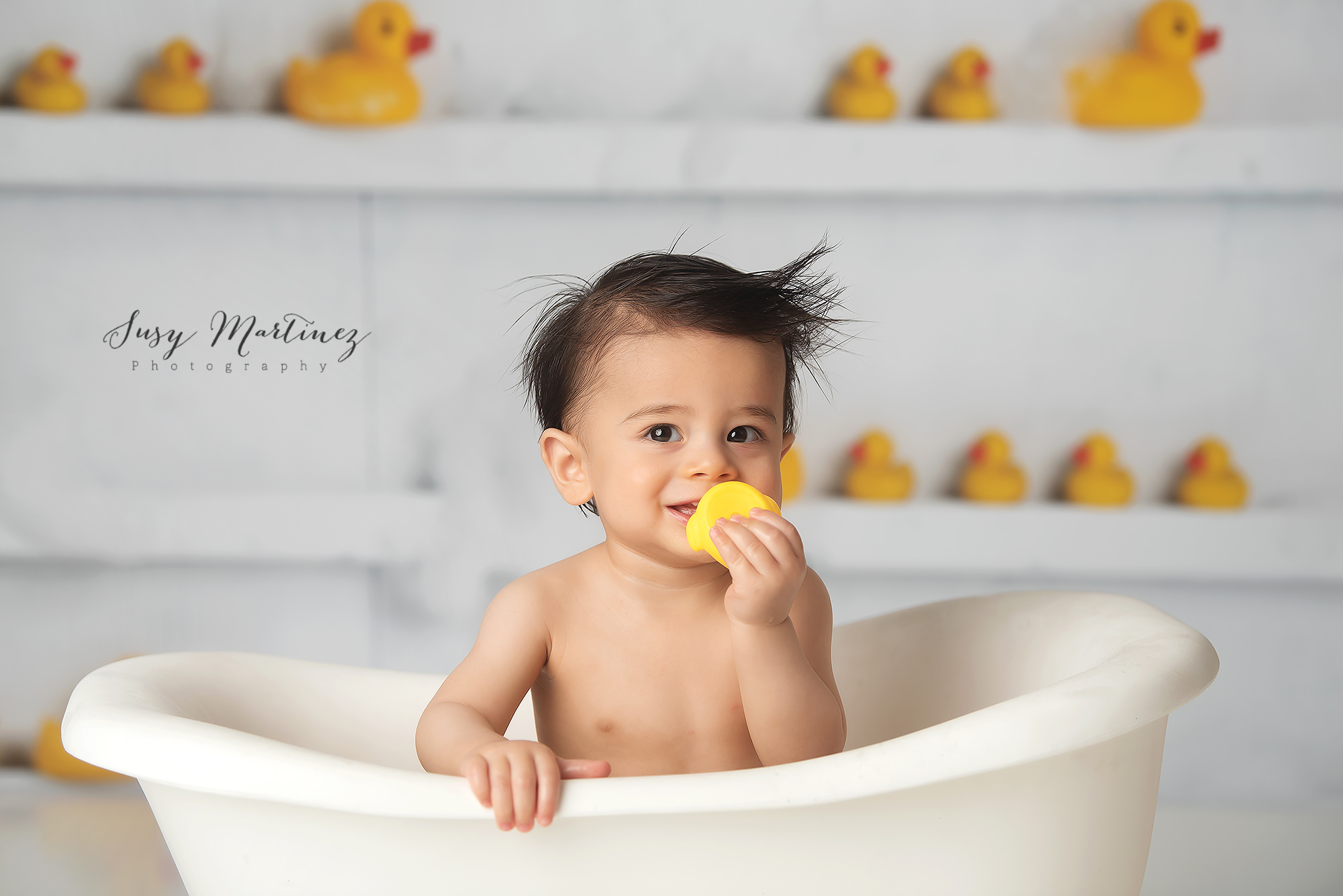 little boy holds rubber duck in tub photographed by Susy Martinez Photography