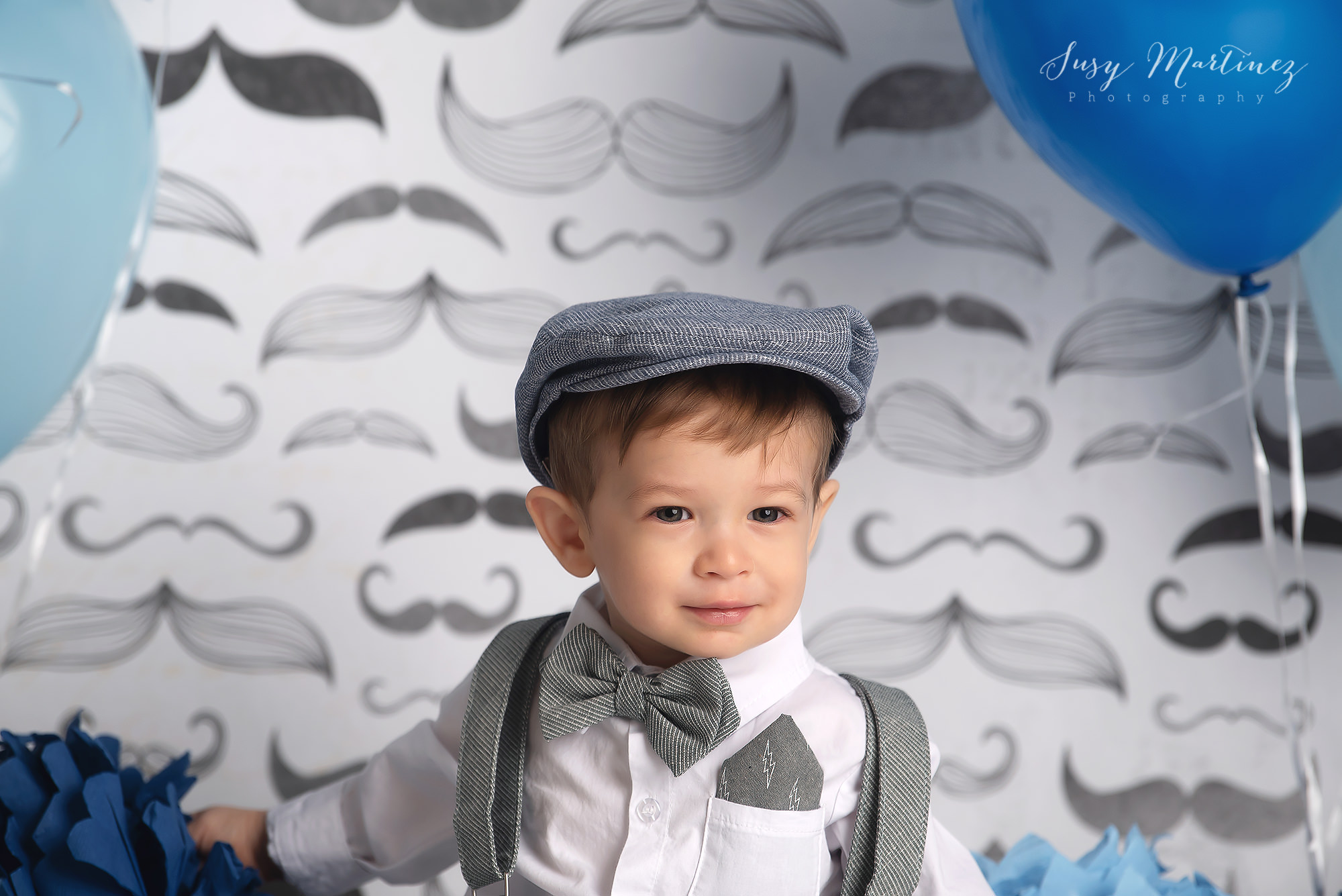 baby poses in front of grey mustache backdrop for first birthday
