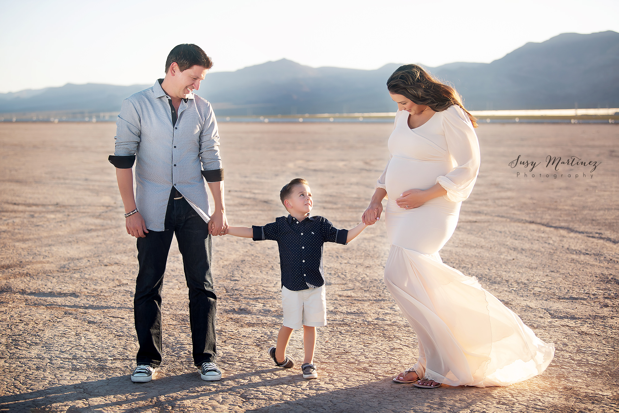 big brother looks up at parents during Dry Lake Bed maternity session with Susy Martinez Photography