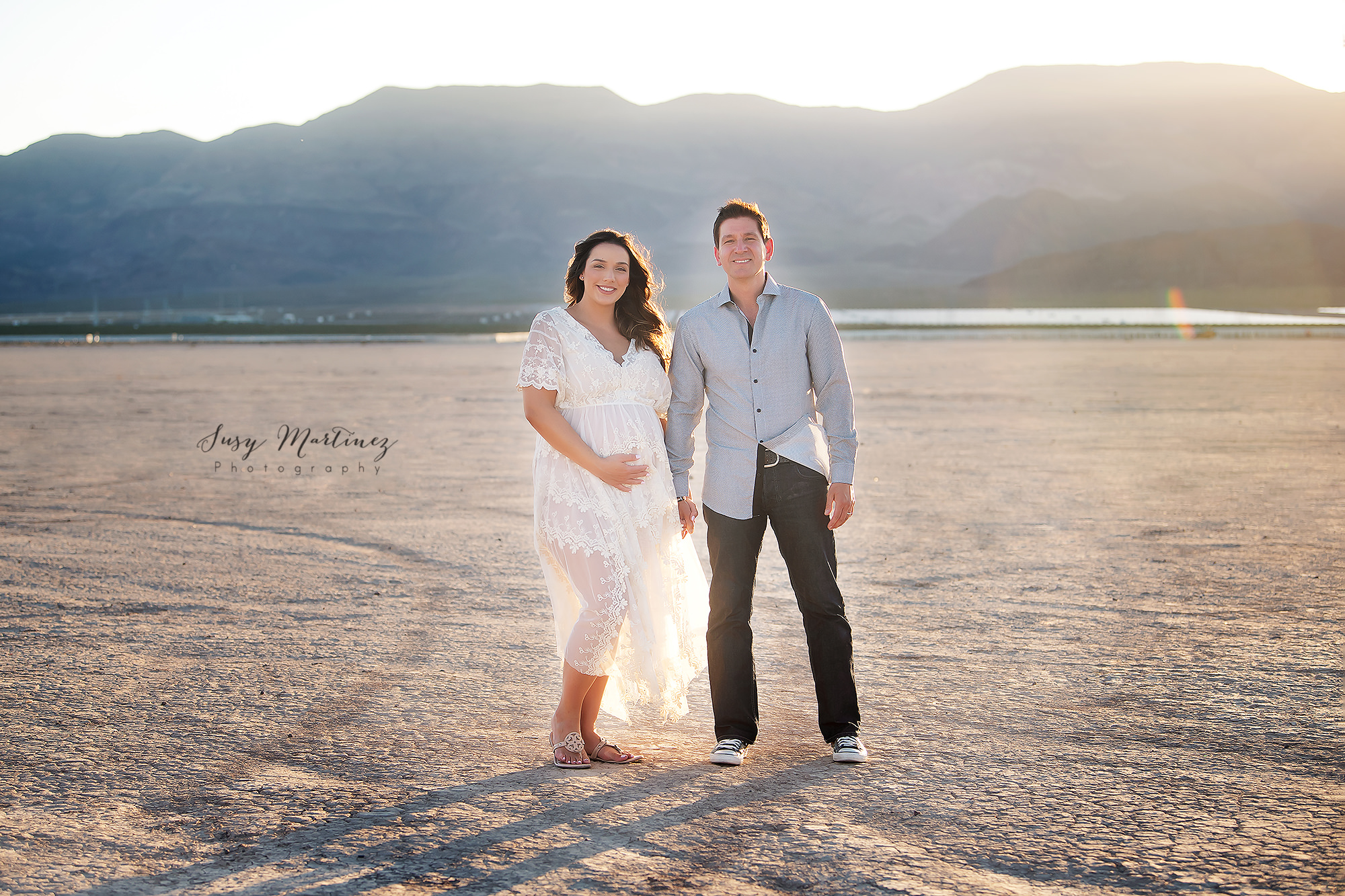 mom holds belly and dad's hand during Dry Lake Bed Maternity Portraits