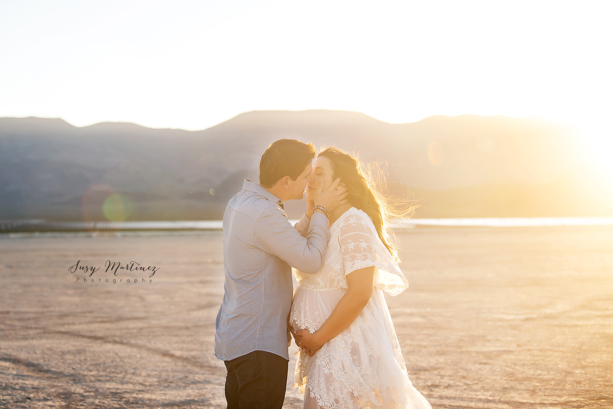 husband kisses wife while she holds baby belly during Dry Lake Bed Maternity Portraits