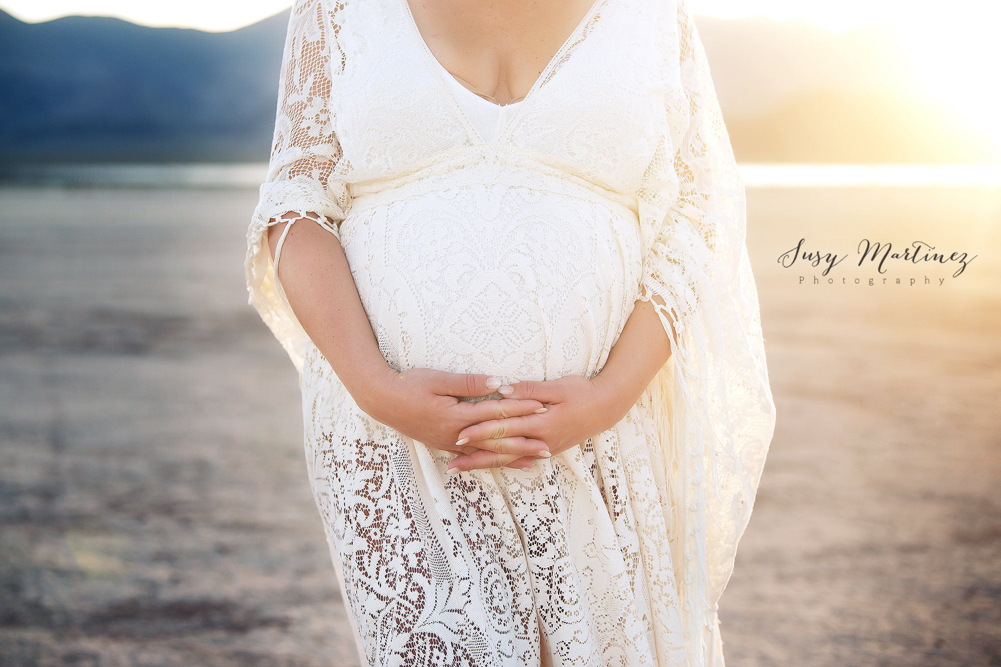 mom holds baby belly wearing lace gown in Dry Lake Bed