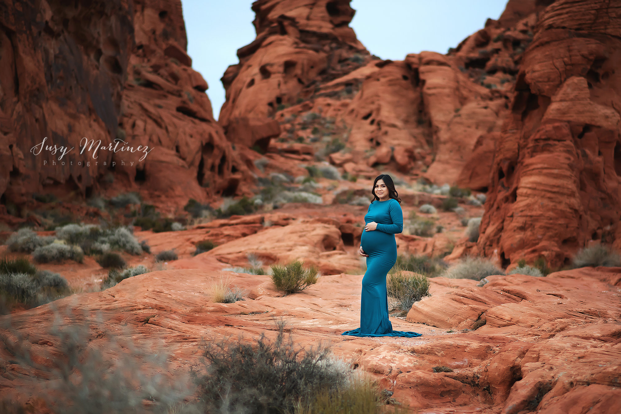 mom in teal dress holds belly standing in Valley of Fire
