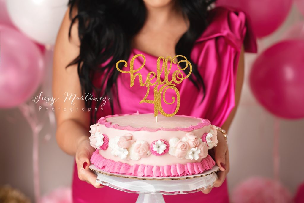 woman holds pink cake with gold topper