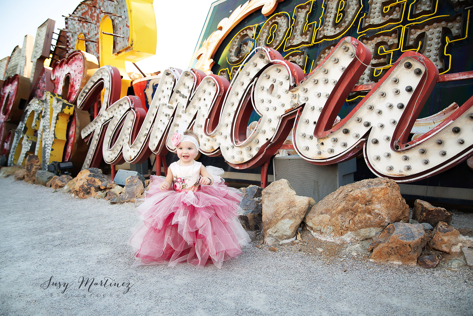 toddler in pink Doll Cake gown poses in front of Las Vegas neon sign