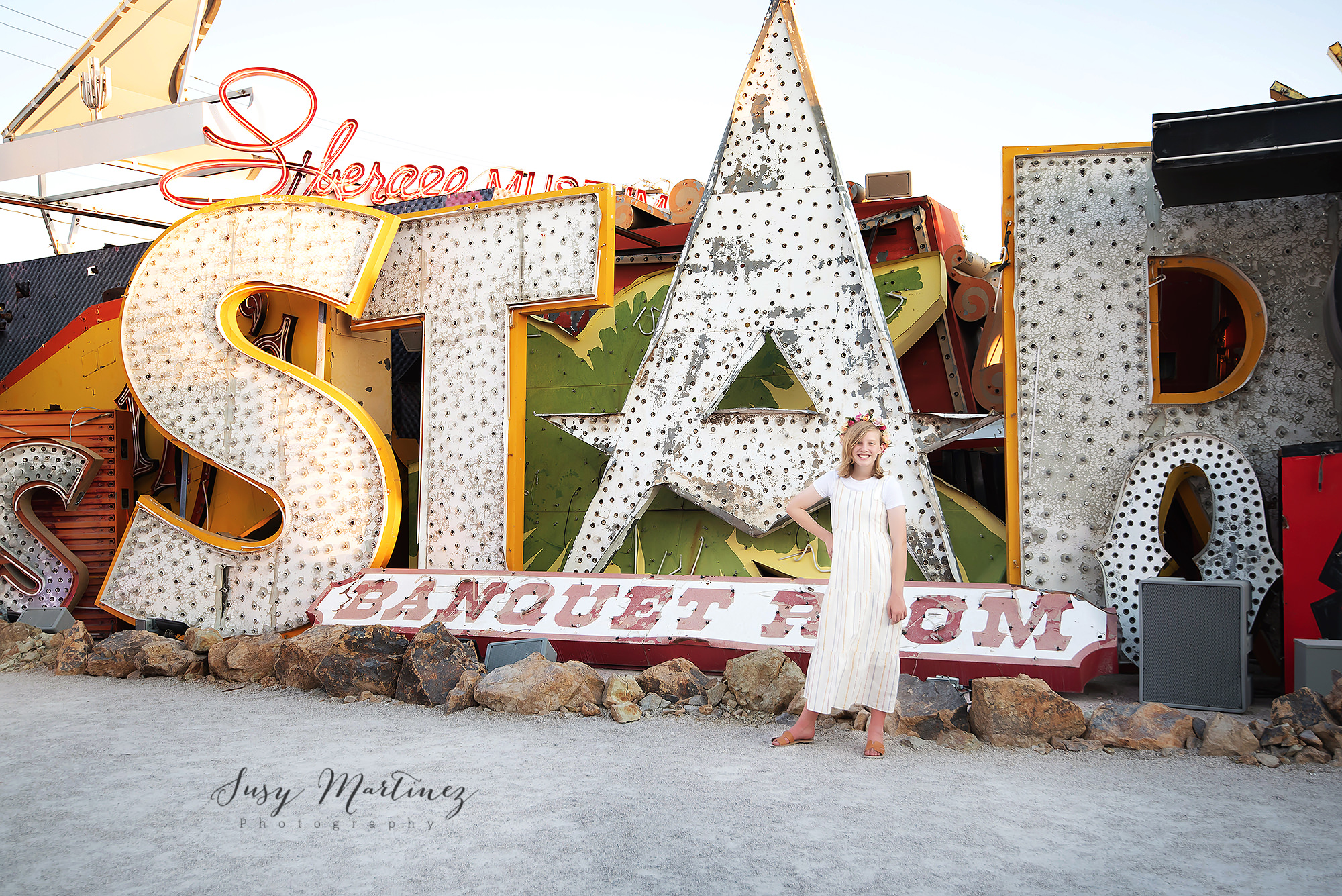 young girl in tan dress poses in front of STAR sign in Neon Boneyard