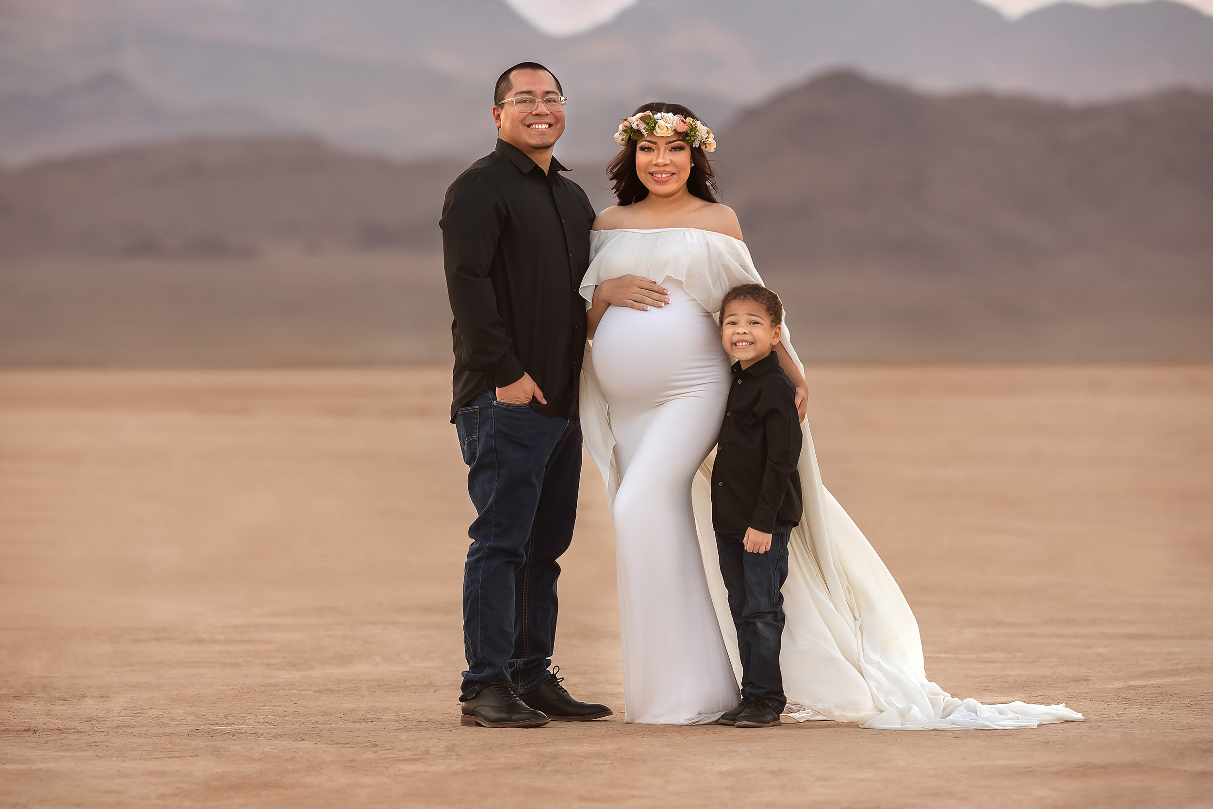 husband poses with wife in white maternity gown during Dry Lake Bed maternity session