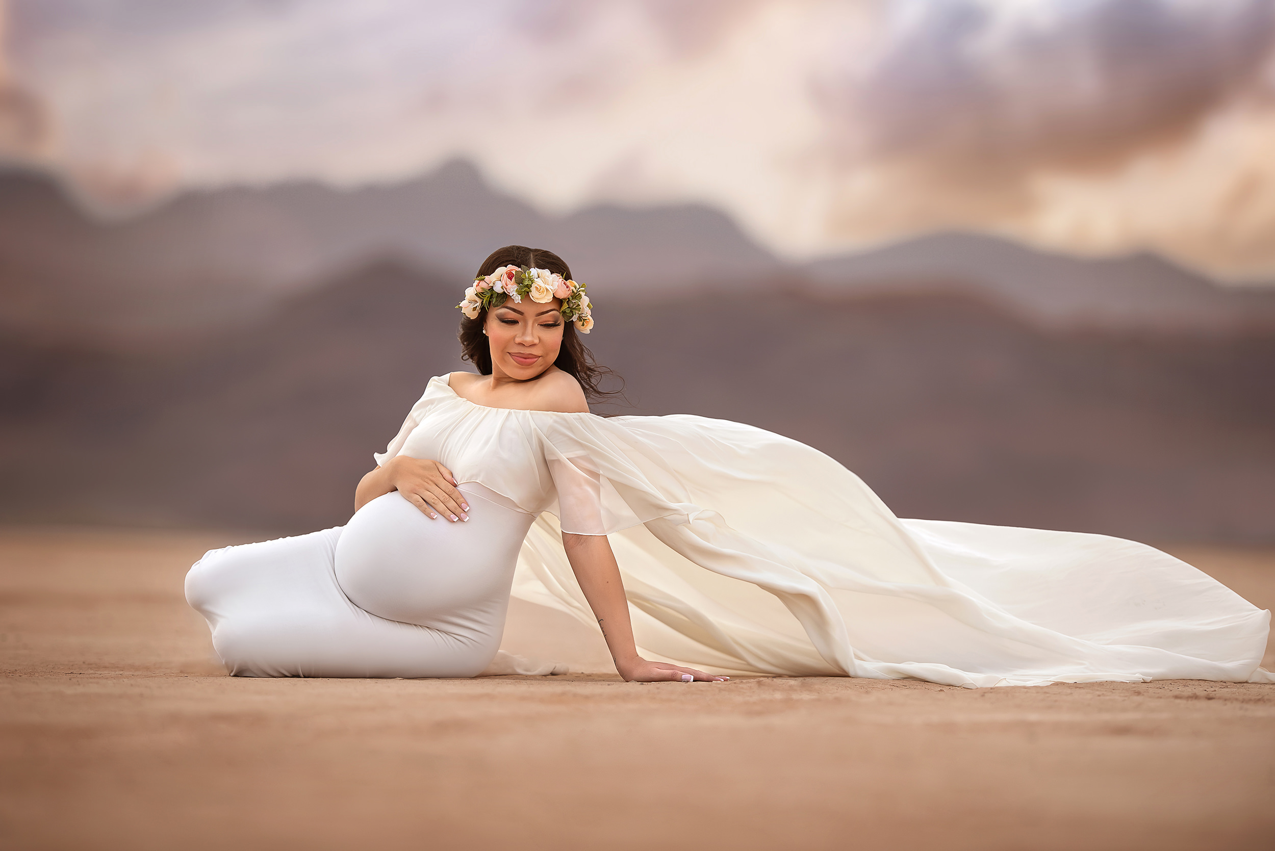 expecting mother sits on side holding belly during Dry Lake Bed maternity session in ivory gown