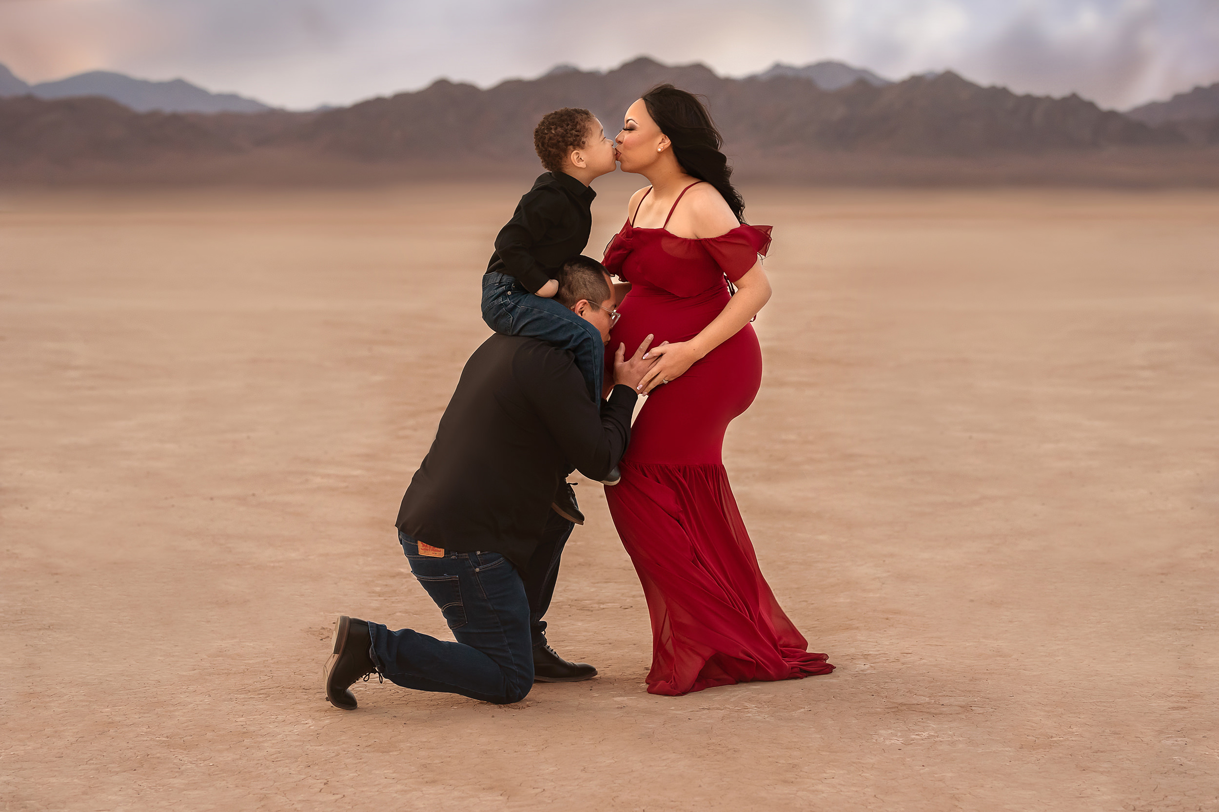 mom kisses son while dad kisses mom's belly during Dry Lake Bed maternity session