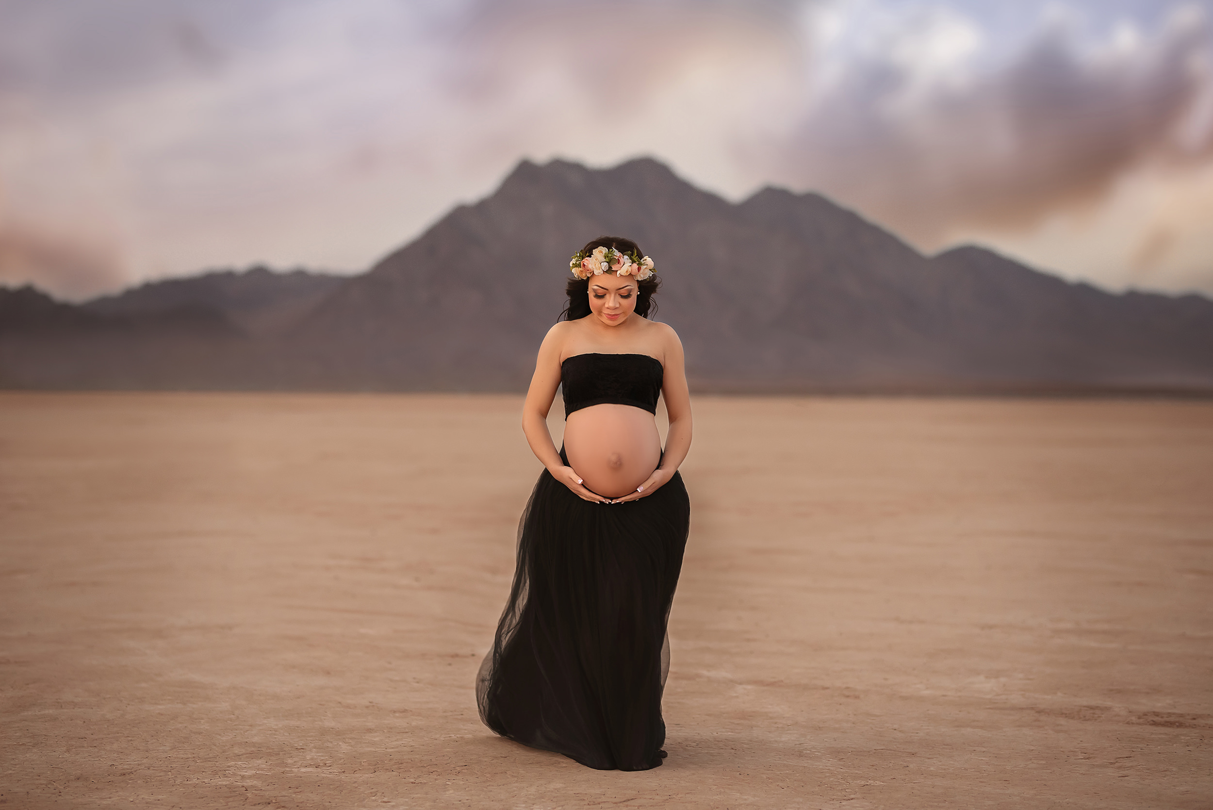 mother in two piece maternity gown and flower crown holds belly during Dry Lake Bed maternity session