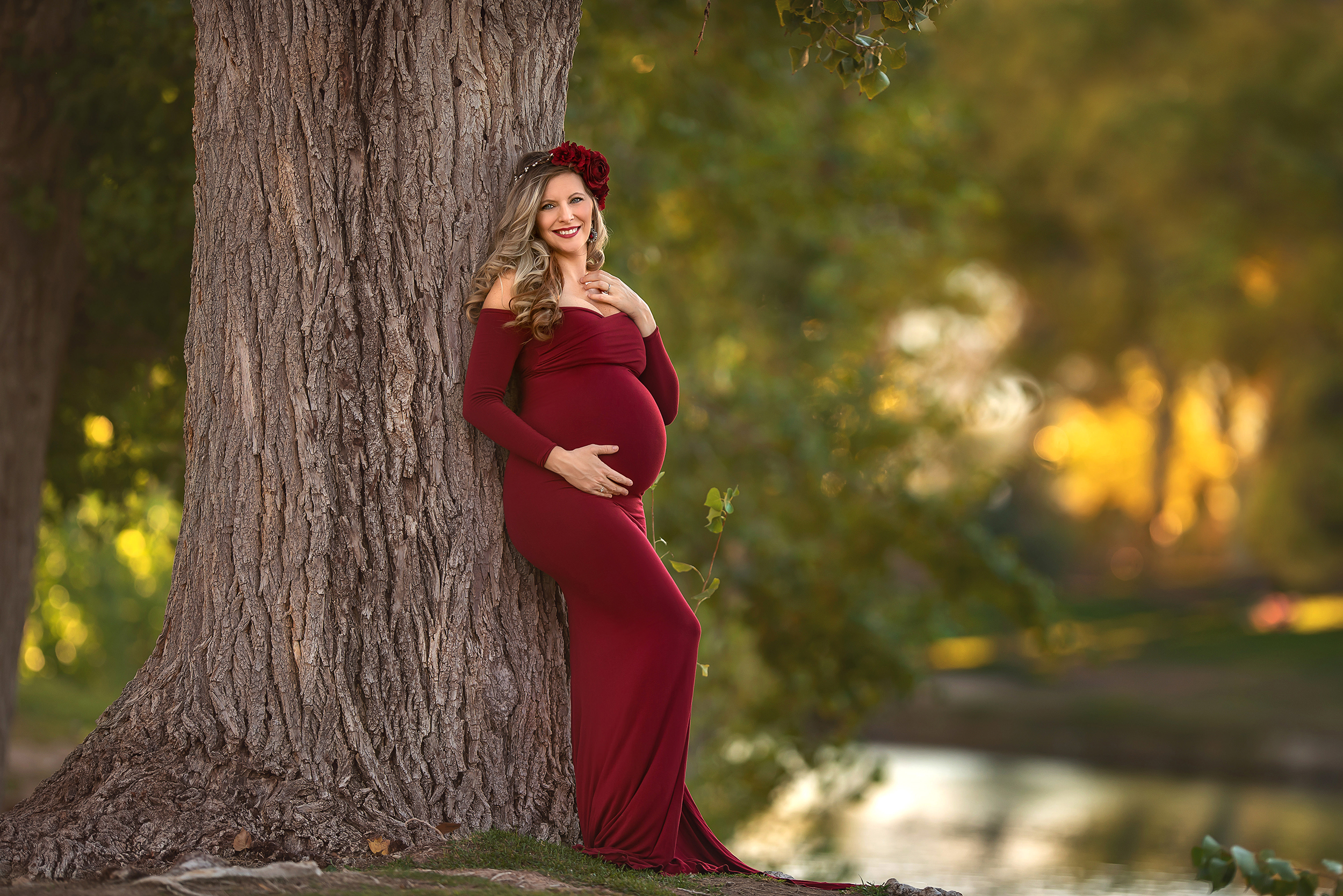 expecting mom in off-the-shoulder red gown leans against tree in Floyd Lamb Park