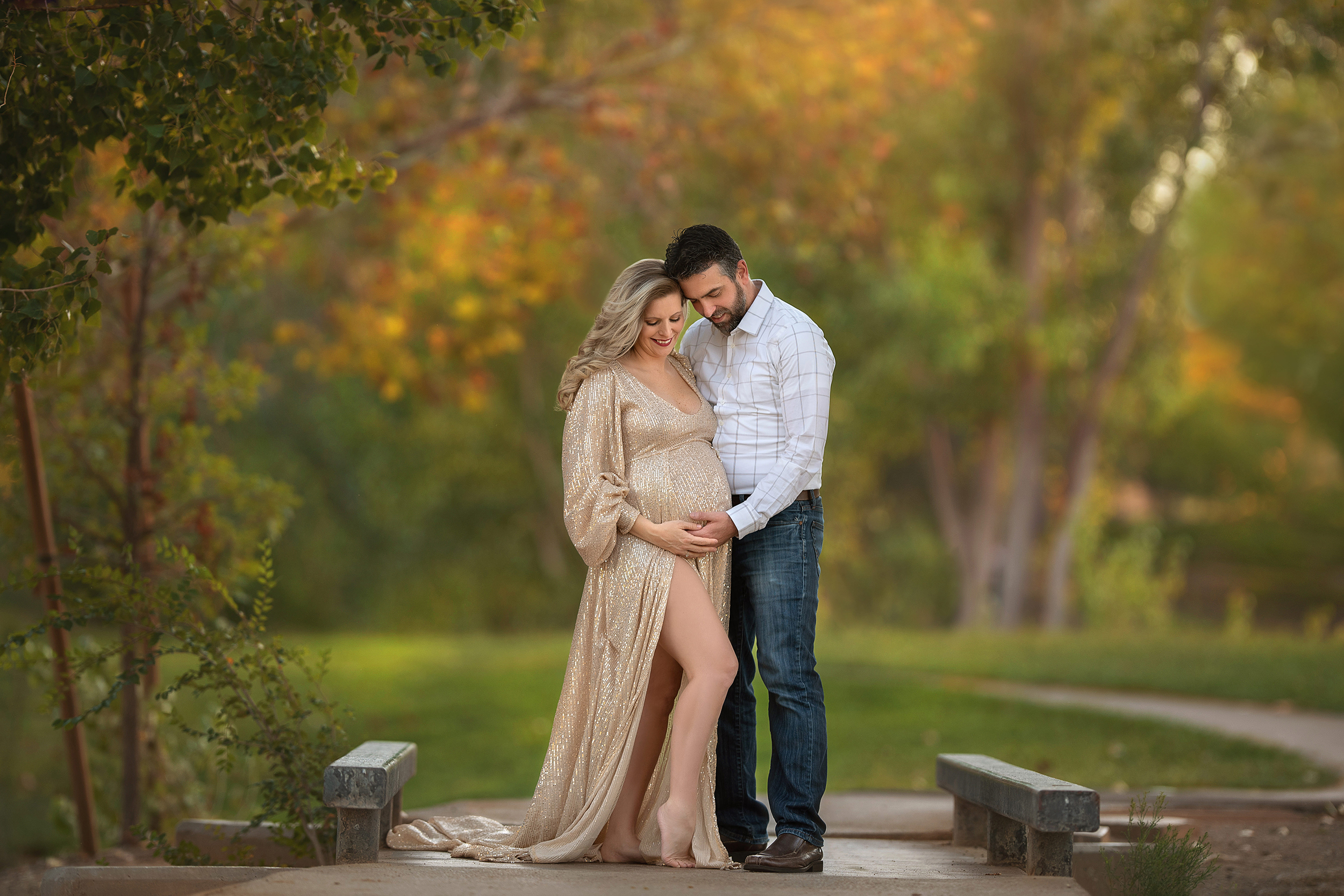 mom stands in gold maternity gown with husband holding baby belly at Floyd Lamb Park