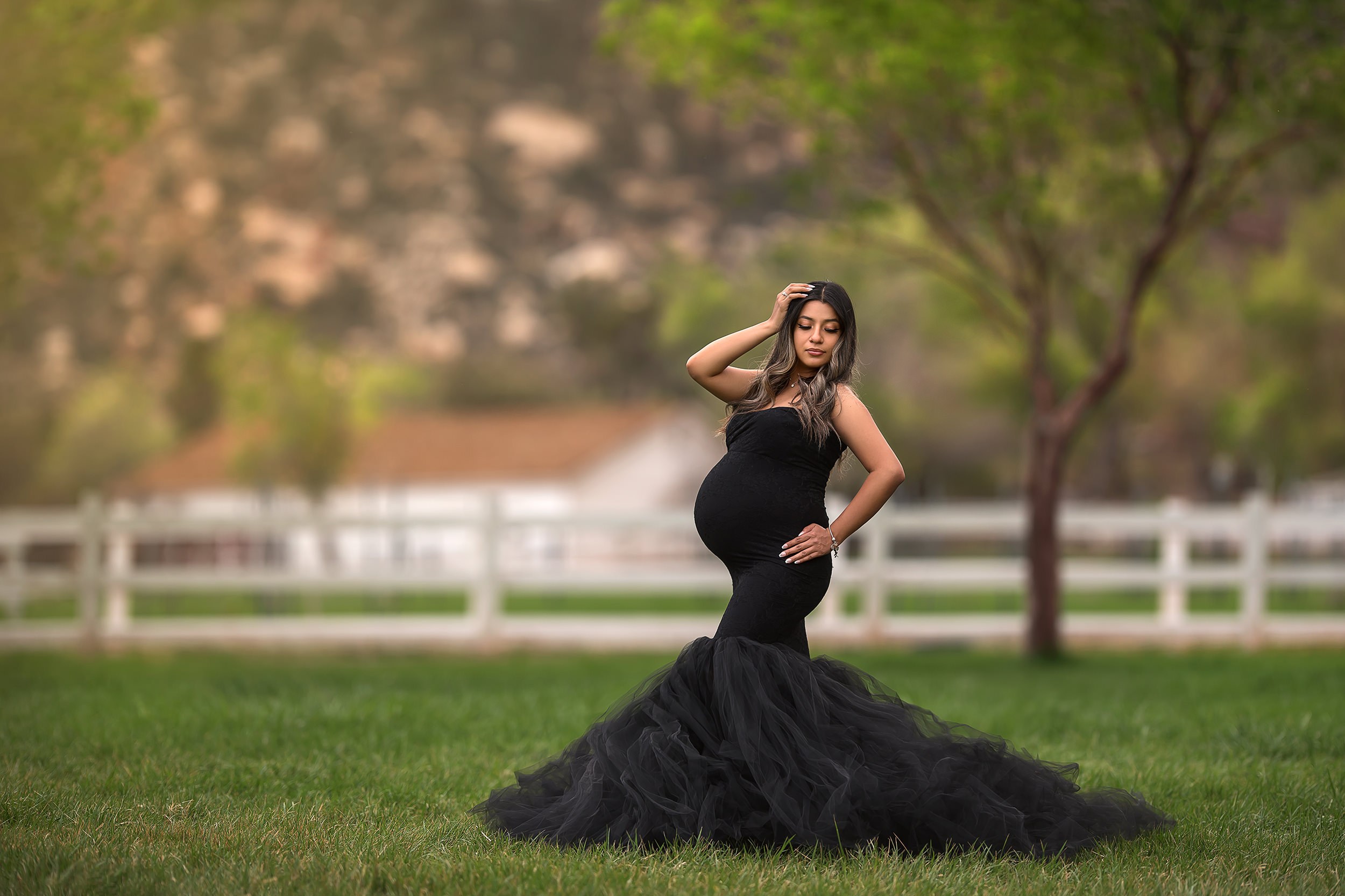 mom stands in black mermaid maternity gown with hand on hip and head