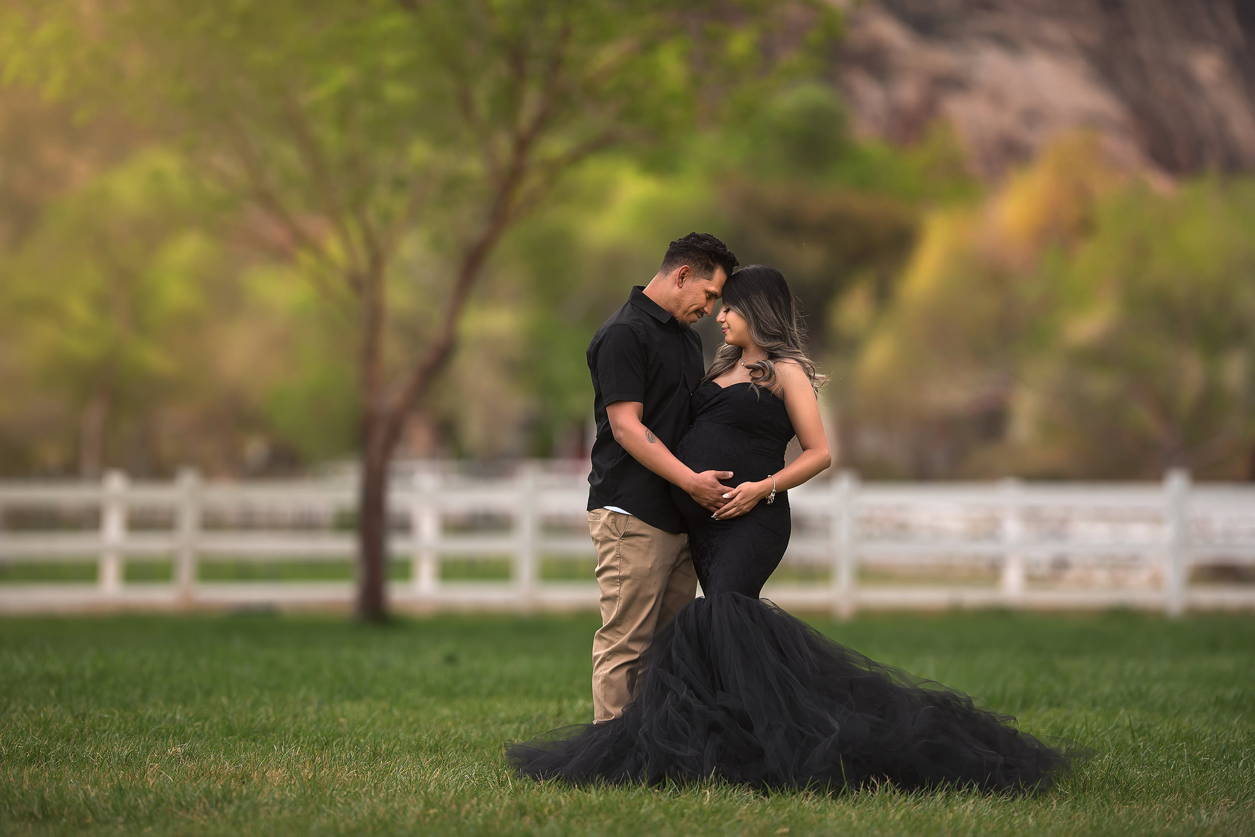 couple stands touching heads while holding baby belly during maternity photos in Las Vegas 