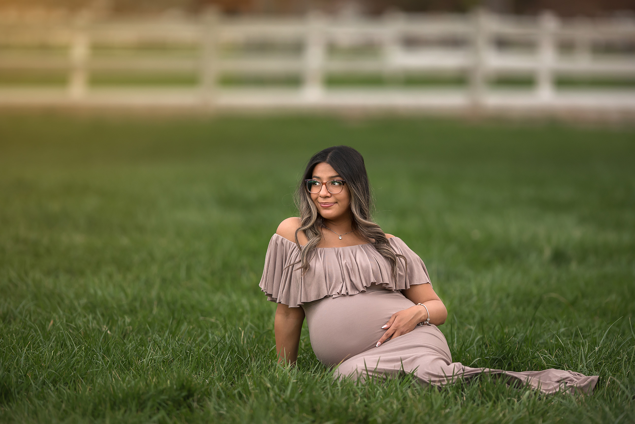 expecting mother sits in grass holding belly during Spring Mountain Ranch Maternity Session