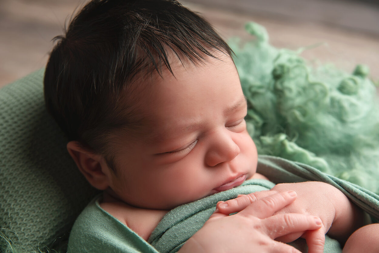 baby boy sleeps in green blanket during newborn portraits 