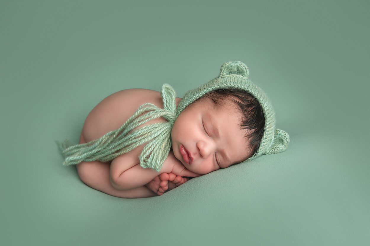 baby lays in green knit cap during Las Vegas studio newborn portraits 